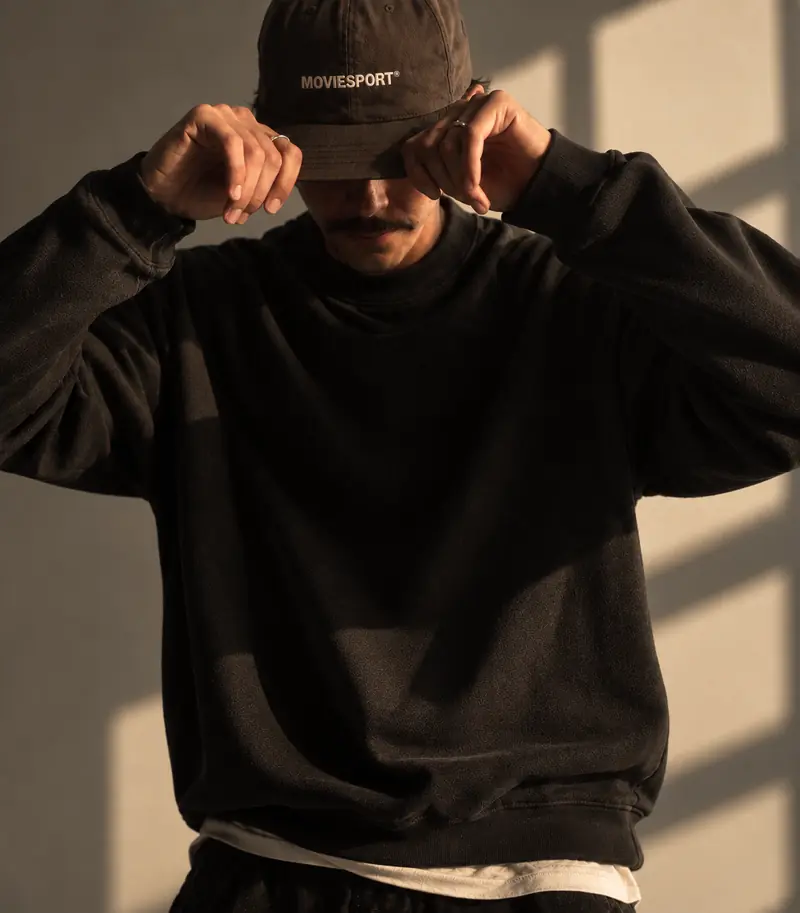 Homme portant une casquette MovieSport, ombres de fenêtre sur un mur crème